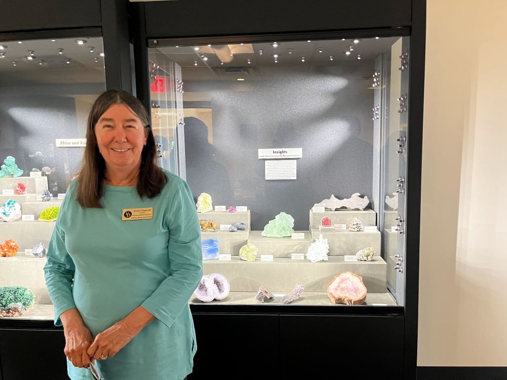Woman facing viewer. Standing in front of case of minerals