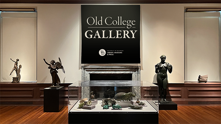 Photo of gallery with large bronze sculptures on either side of a fireplace, two windows with sculptures in the window sills, and a case in the fore ground with small sculptures and mineral specimens.