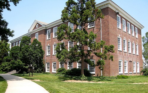 Three-story brick building with white trim. Seen from a diagonal view. Trees in front.