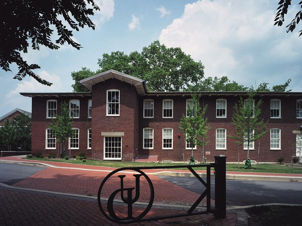 Exterior of a two-story brick building, windows with white trip. UD gate in foreground