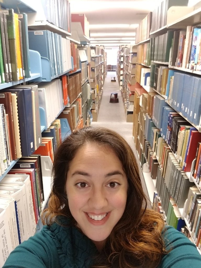 Mariana takes a selfie with "her shelf" in the Morris Library.