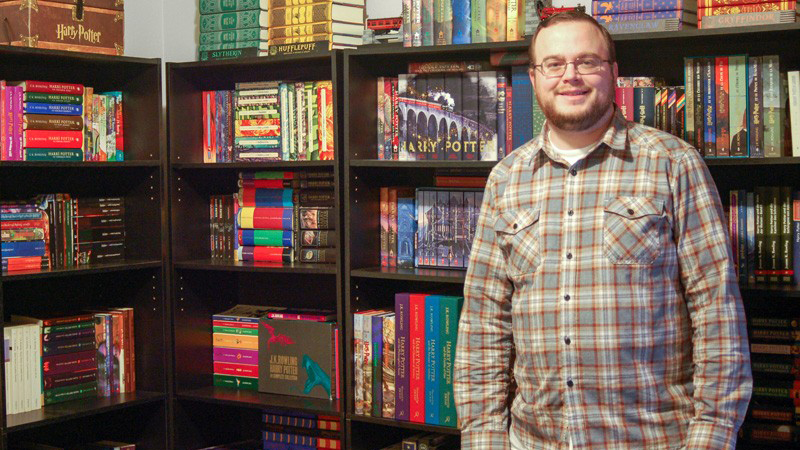 Sean McAllister stands in front of bookshelves displaying his Harry Potter collection.