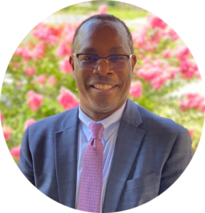 Headshot of a man in a suit in front of pink flowers