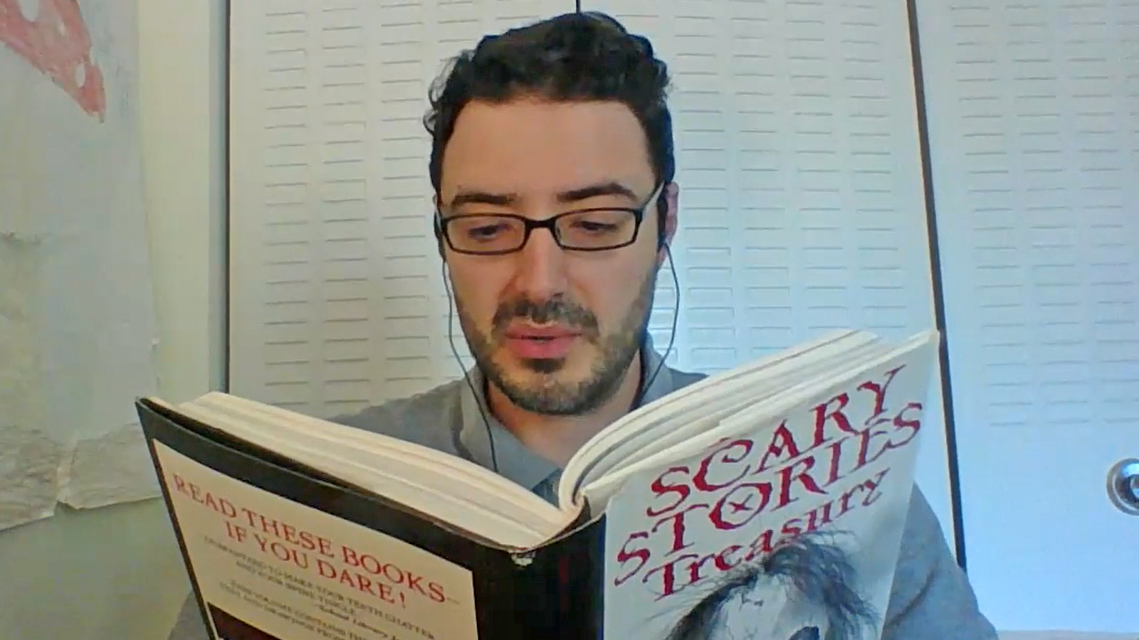 A man looking down as he reads a book "Scary Stories Treasury"