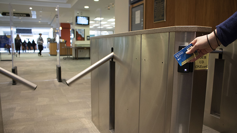 The entrance turnstiles to Morris Library opening as someone taps their UD ONEcard to get in.