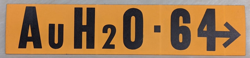 A goldish yellow bumper sticker that reads "AuH20 64"