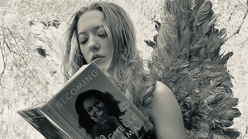 A back and white image of a young girl with wings reading an open book.