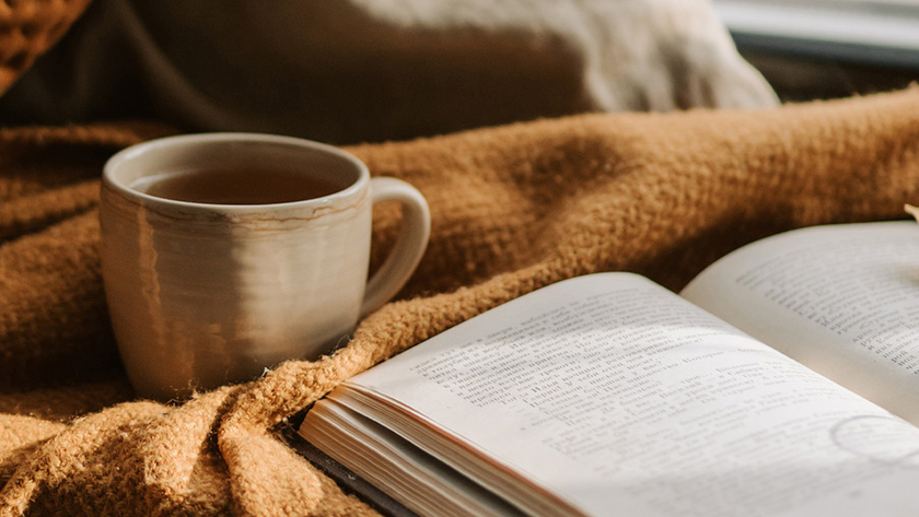 An open book and a mug on top of a cozy blanket.