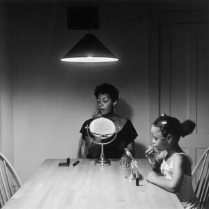 Black and white photo of a female adult and child putting on makeup at a table.