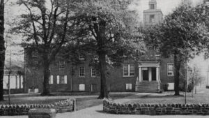 black and white photograph of a building surrounded by trees and with a stone walkway.