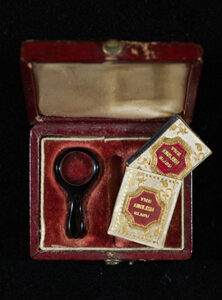 The casing for a tiny book. The interior of the case is velvet and includes a mini magnifying glass alongside the book.