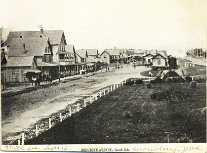 A black-and-white postcard that shows a dirt road line with houses and grassy areas.
