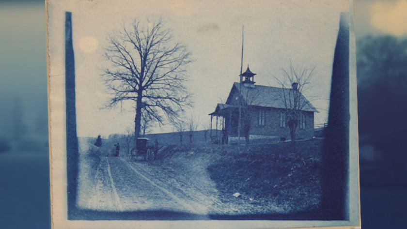 Cyanotype image of a single room school house next to a tree.