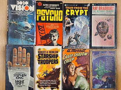 Eight bound paperbacks with titles like "Psycho", "Tales from the Crypt" and "Starship Troopers" lie on a table top.