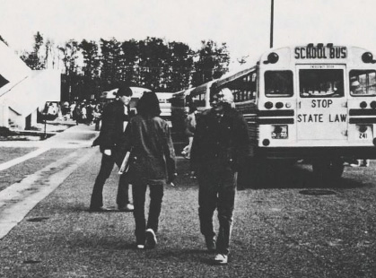 Black and white photo of students walking in front of a parked school bus.