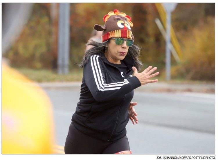 A person is seen running in a race while wearing a turkey shaped knit cap.