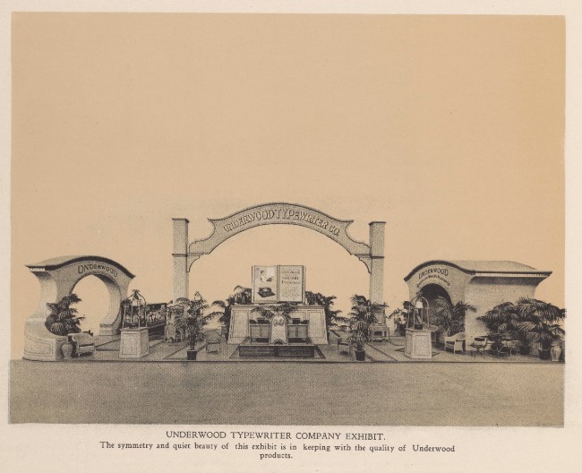 A sepia photograph of the symmetrical Underwood Typewriter Company pavilion. The setup features a large ornamental arch stretching over a display with giant open book props, flanked by palm plants and comfortable sitting areas.
