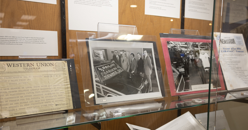 A glass display case featuring historical archival materials, including a Western Union telegram and a black-and-white photograph of workers posing beside a car with a sign reading "4,000,000th PRODUCED AT NEWARK, DEL."