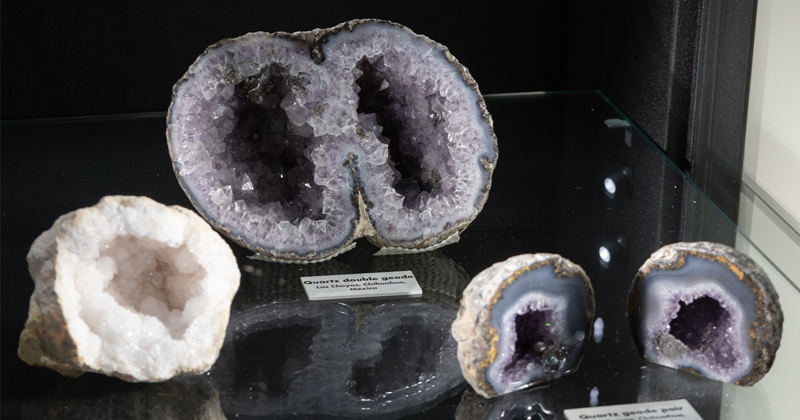 A close-up view of sliced quartz geodes on a reflective glass shelf, highlighted by a large double geode with purple amethyst crystals in the center alongside smaller split geodes.