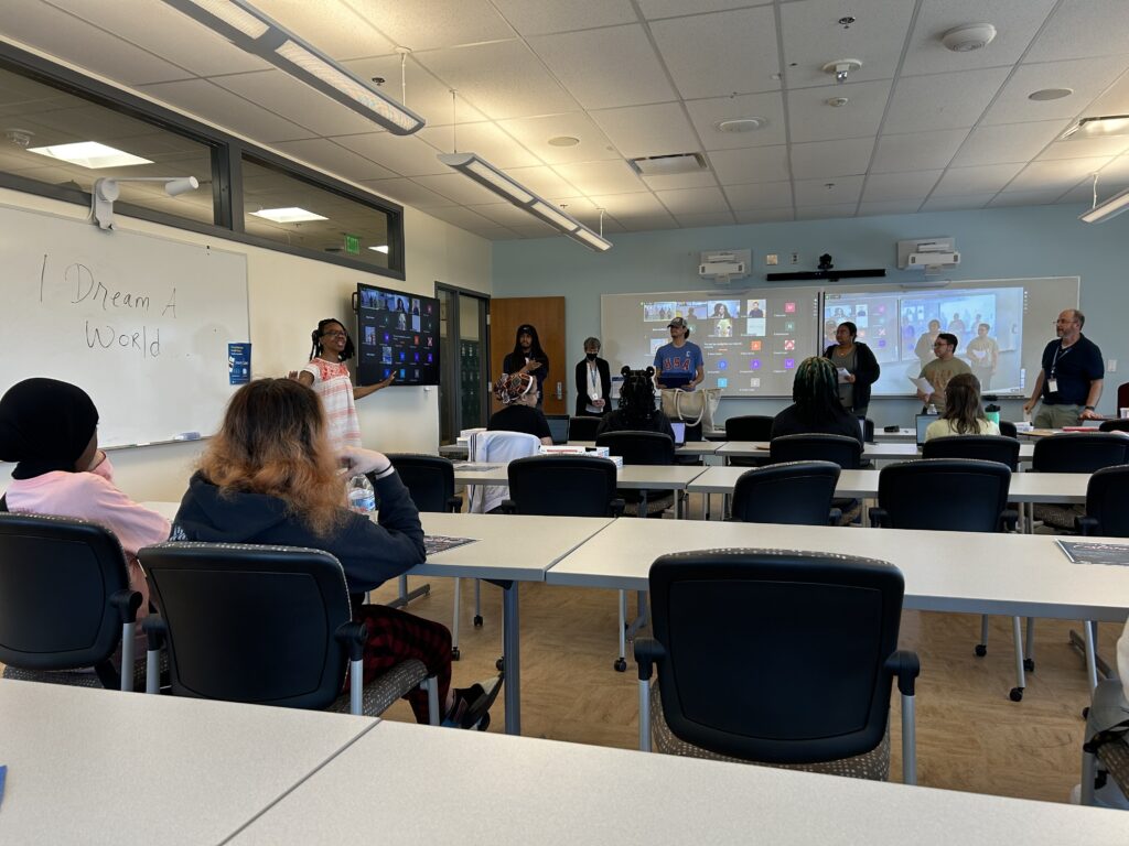 Dr. Currie leads a workshop as part of the UD Associate in the Arts Program's Spring 2024 Seminar Series on May 7, 2024. The projectors show participants joining the seminar via Zoom. The whiteboard reads: "I dream a world."